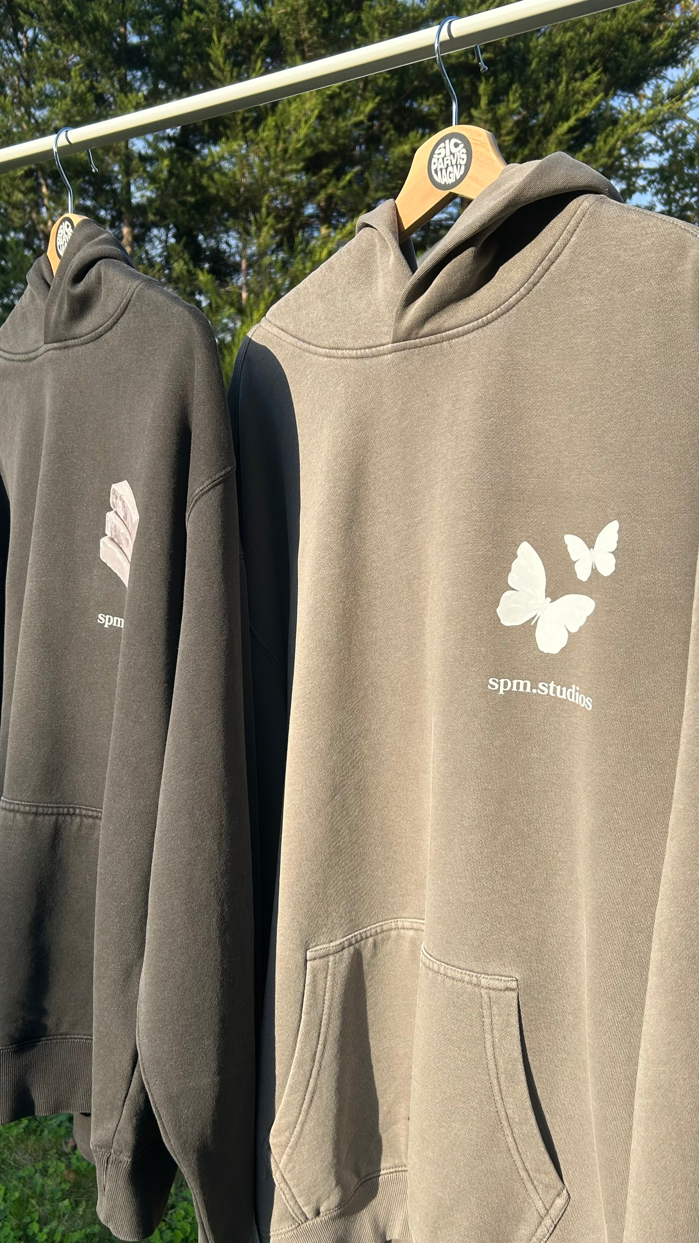 Two hoodies hanging on a rack with butterfly designs and text.